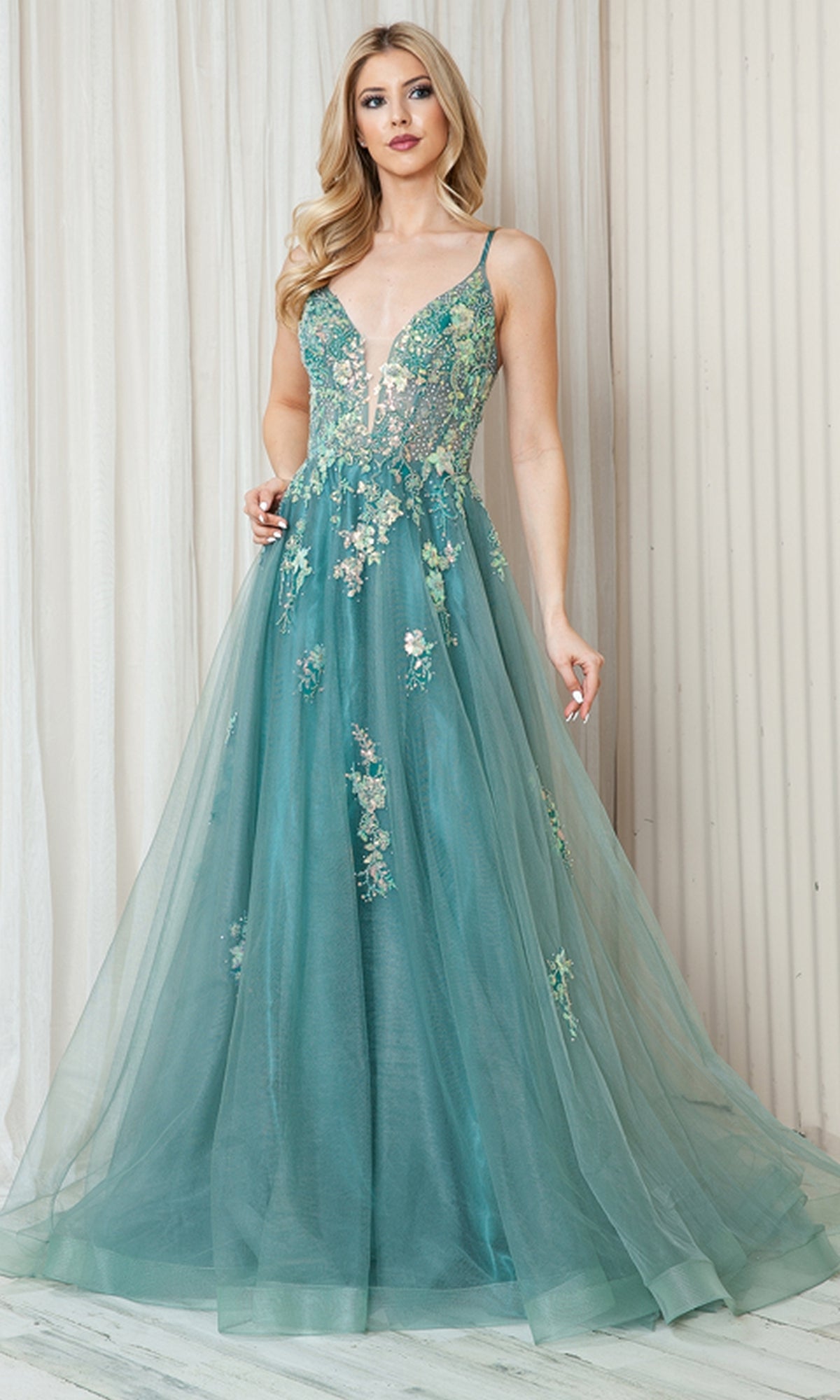 A woman in the Floral-Embellished Pastel Prom Ball Gown TM1003 stands against a light-colored, textured wall.
