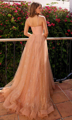 A woman in the Amelia Couture Corset Glitter Prom Dress TM1022 stands on a terrace with her back to the camera, facing blooming pink flowers, her peach-colored gown shimmering in the soft light.