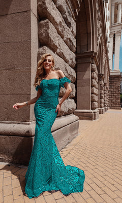A woman in the Long Glitter-Lace Prom Dress, Tina Holly TW024, stands smiling against a stone building with arched architecture on a sunny day.