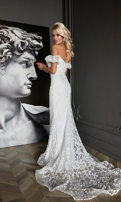 A woman in the Off-Shoulder White Formal Dress: Tina Holly Tk024W with a floral pattern stands near a large classical sculpture artwork in a dimly lit room with wooden floors.