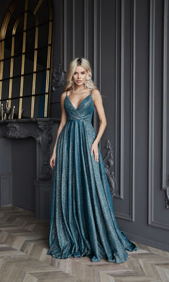 A woman in a shimmering teal Long Glitter A-Line Prom Dress, Tina Holly TW079, with thin straps stands indoors against an ornate gray wall and a decorative fireplace.
