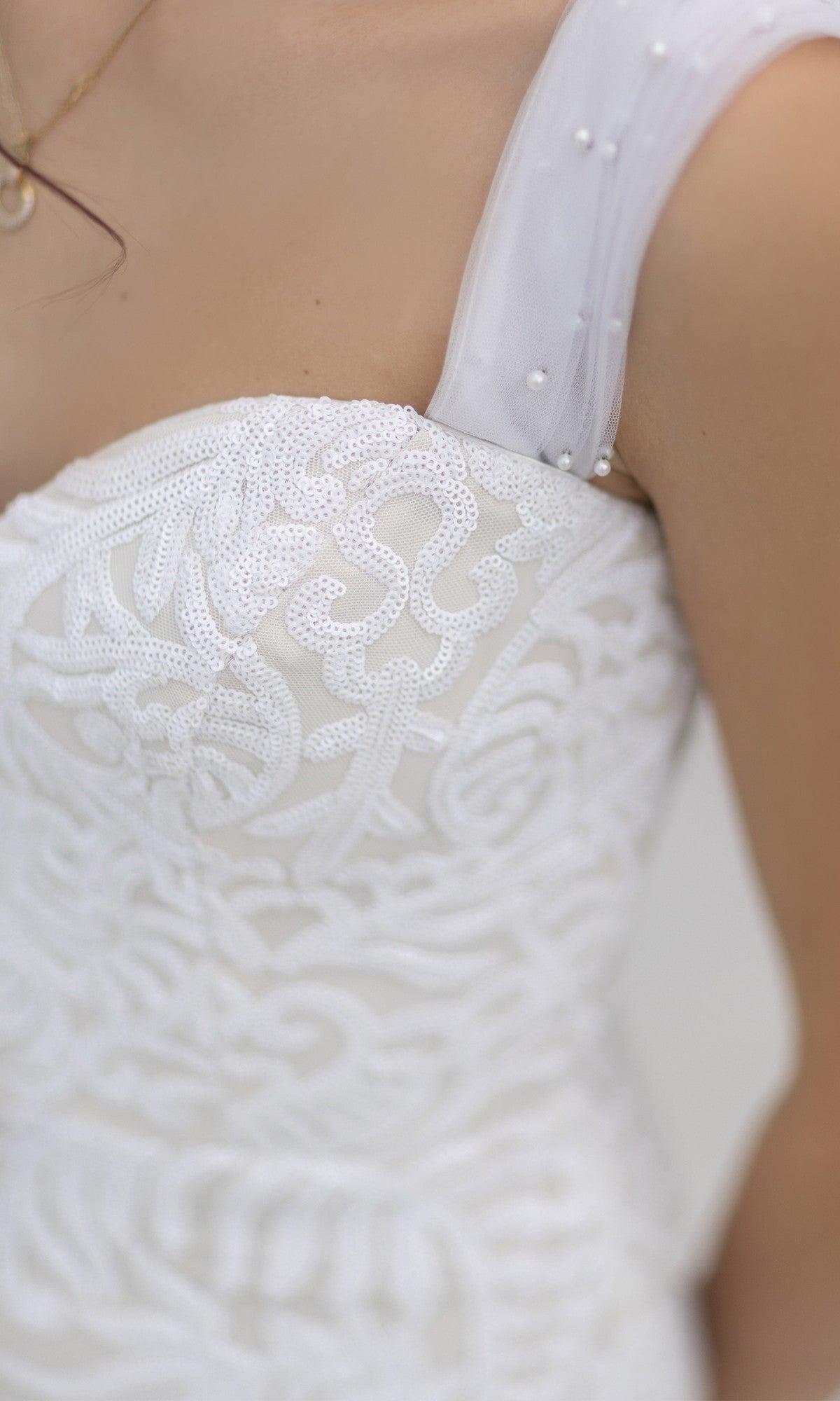 Close-up of a woman wearing the Off-Shoulder White Bridal Gown: Tina Holly TW103, featuring sheer, pearl-embellished straps and delicate white lace.