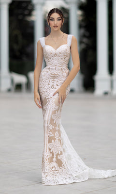 A woman stands outdoors on a stone patio in the Off-Shoulder White Bridal Gown: Tina Holly TW103, a fitted, sleeveless lace gown with floral patterns, framed by columns and lush greenery.