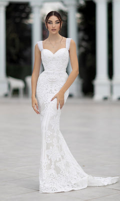 A woman stands outdoors before white columns wearing the Tina Holly TW103, an off-shoulder, floor-length white bridal gown.