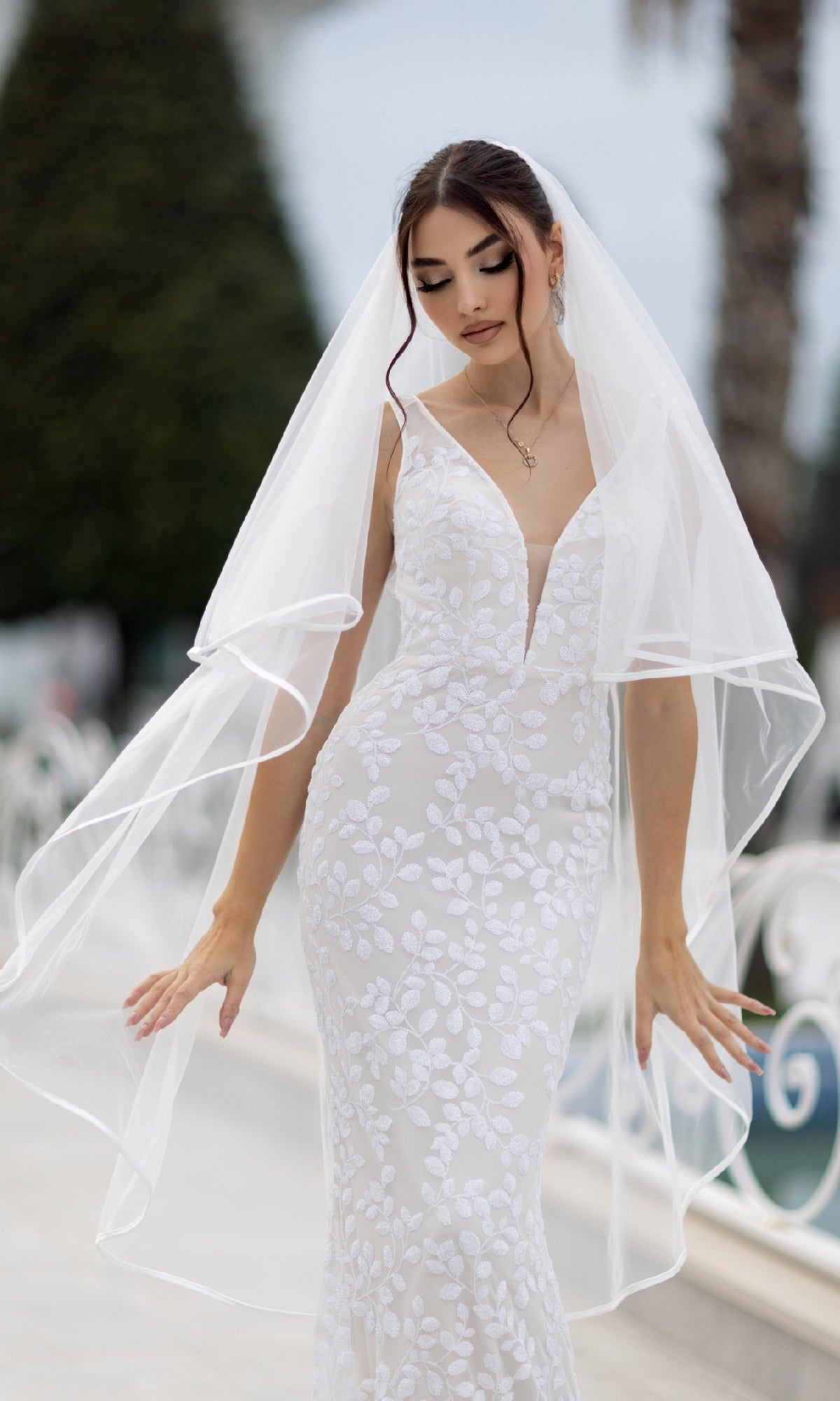A woman in the Long White Sequin Formal Dress: Tina Holly TW108 stands outdoors, wearing a veil and looking down with her hands slightly raised.