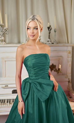 A woman wears the Long Formal Dress: Tina Holly TW603, featuring a strapless taffeta design with an a-line skirt and detachable bow, as she stands before a white upright piano decorated with candles and ornate accents.
