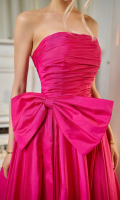 Someone wearing the Long Formal Dress: Tina Holly TW603—a strapless bright pink taffeta evening gown with a ruched fitted bodice and a large detachable bow at the waist.