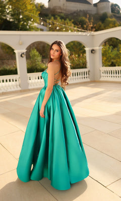 A woman in the Tina Holly TW608 long formal dress with a corset bodice stands outdoors on a sunlit terrace, glancing over her shoulder at the camera.