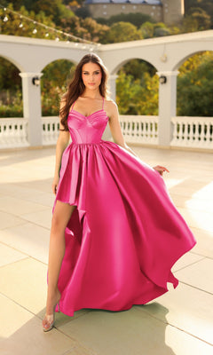 A woman wears the Long Formal Dress: Tina Holly TW608 in fuchsia pink, featuring a corset bodice and high slit, as she stands on a sunlit outdoor terrace with white columns and lush greenery.