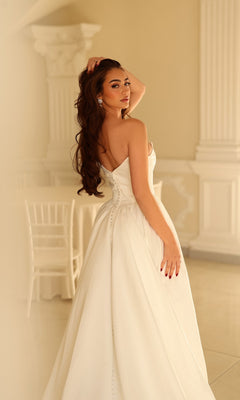 A person wearing a Long Wedding Dress: Tina Holly TW622, a strapless, floor-length white satin bridal gown with a button-up back.