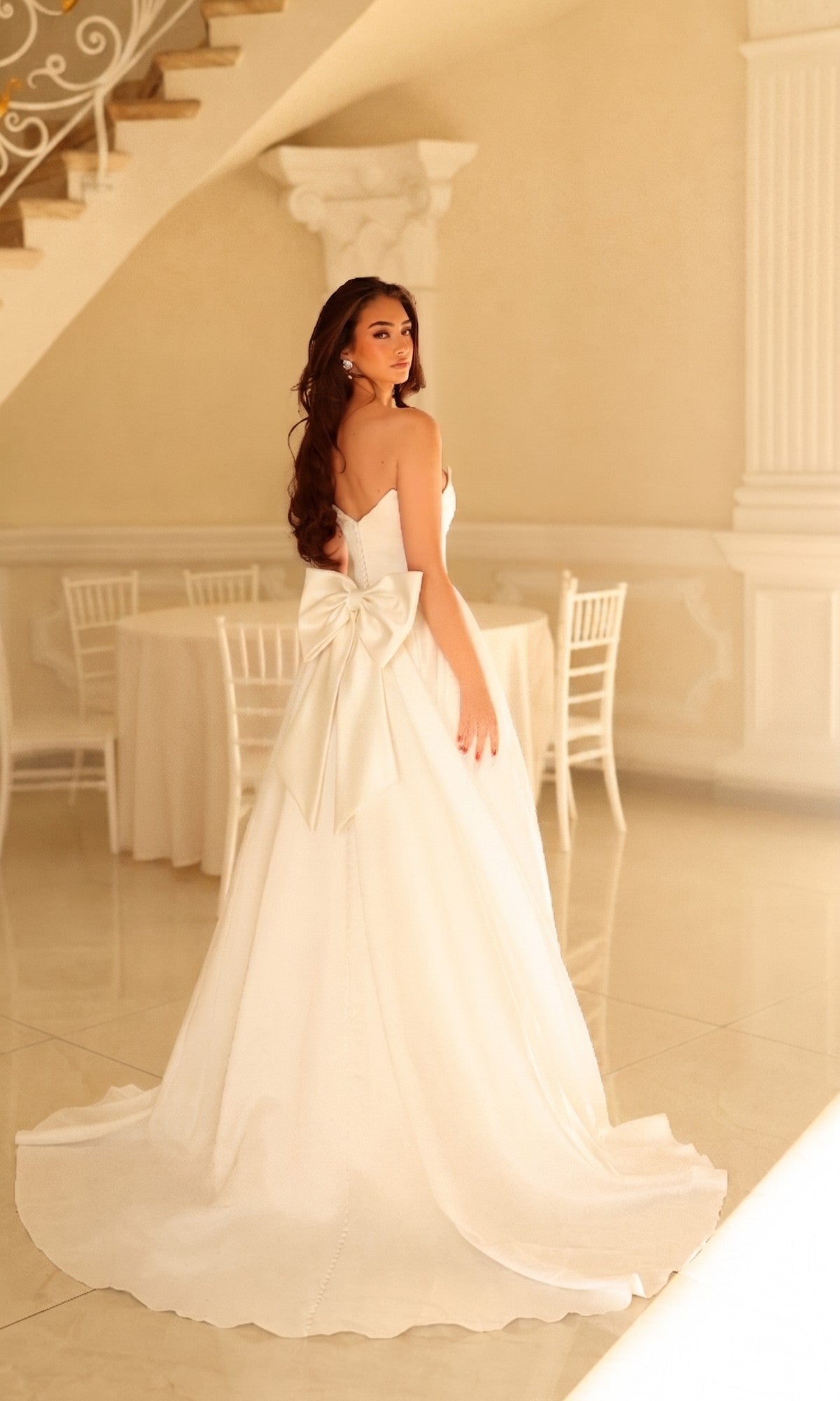 A woman wearing the Long Wedding Dress: Tina Holly TW622, a strapless A-line gown featuring a large bow on the back and a floor-length train.