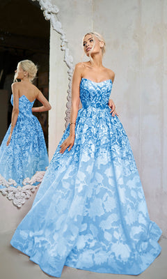 A woman in a floral blue Long Formal Dress (Tina Holly TW624), strapless and floor-length, stands before a mirror with her hair in an elegant updo.