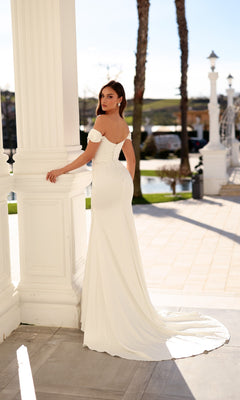 A woman in a floor-length white Tina Holly TW628 wedding dress with a sweetheart neckline and train, standing beside a large white column.