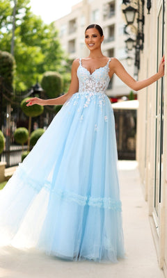 A woman stands outdoors, smiling with one hand on a wall, wearing the Tina Holly TY405 long formal dress in pastel blue, featuring a corset bodice with floral embroidery and a flowing tulle skirt.