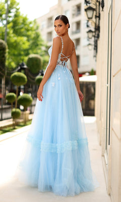 A woman in the Tina Holly TY405 long formal dress, featuring a pastel blue tulle A-line skirt and lace-up corset bodice, stands on a sunlit walkway outdoors, facing away and looking over her shoulder.
