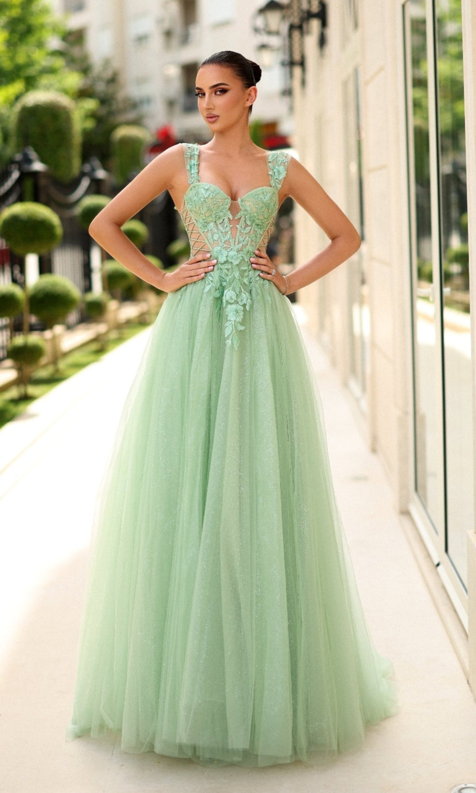 A woman stands outside in the Tina Holly TW500 long prom dress, featuring a light green, floor-length skirt, a fitted corset bodice, floral lace embroidery, and an elegant sleeveless design.