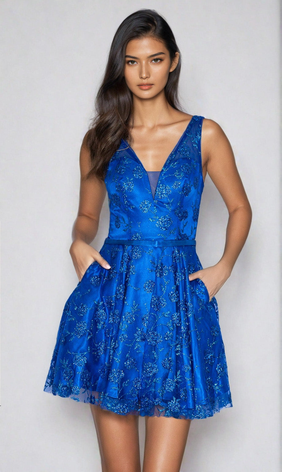 A woman faces forward in the Floral-Glitter V-Neck Short Homecoming Dress 9202, royal color, featuring a sleeveless design, floral patterns, pockets, and a v-neckline against a plain light background.