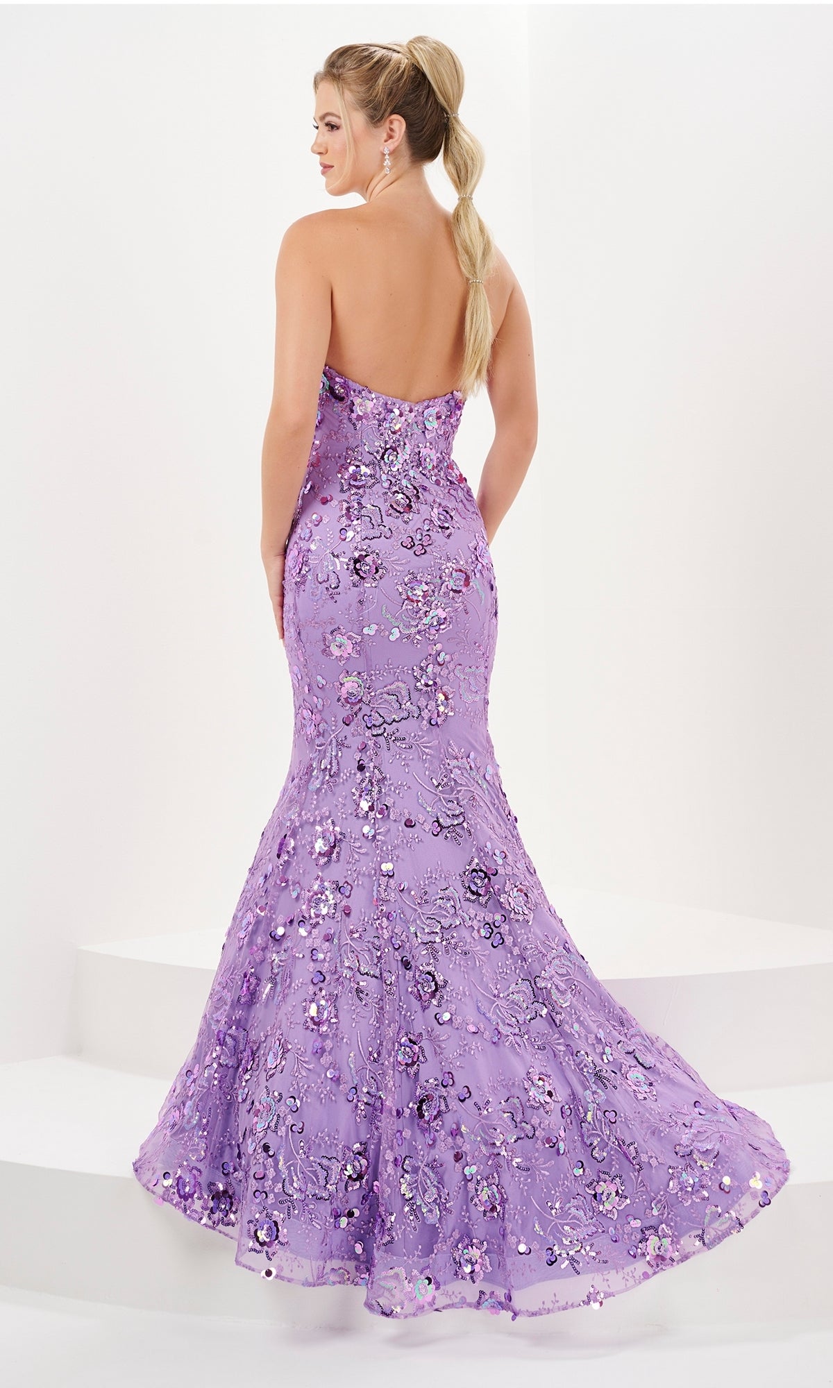 A woman poses with her back to the camera in the Long Prom Dress 16052 by Tiffany, a strapless, floor-length lavender sequin gown, set against a plain white background.