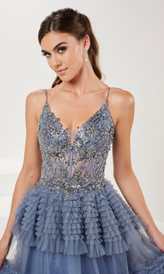A woman models the Long Prom Dress 16054 by Tiffany—a silver floral embellished A-line ball gown with spaghetti straps, layered ruffles, and an embellished V-neck—standing against a light background.