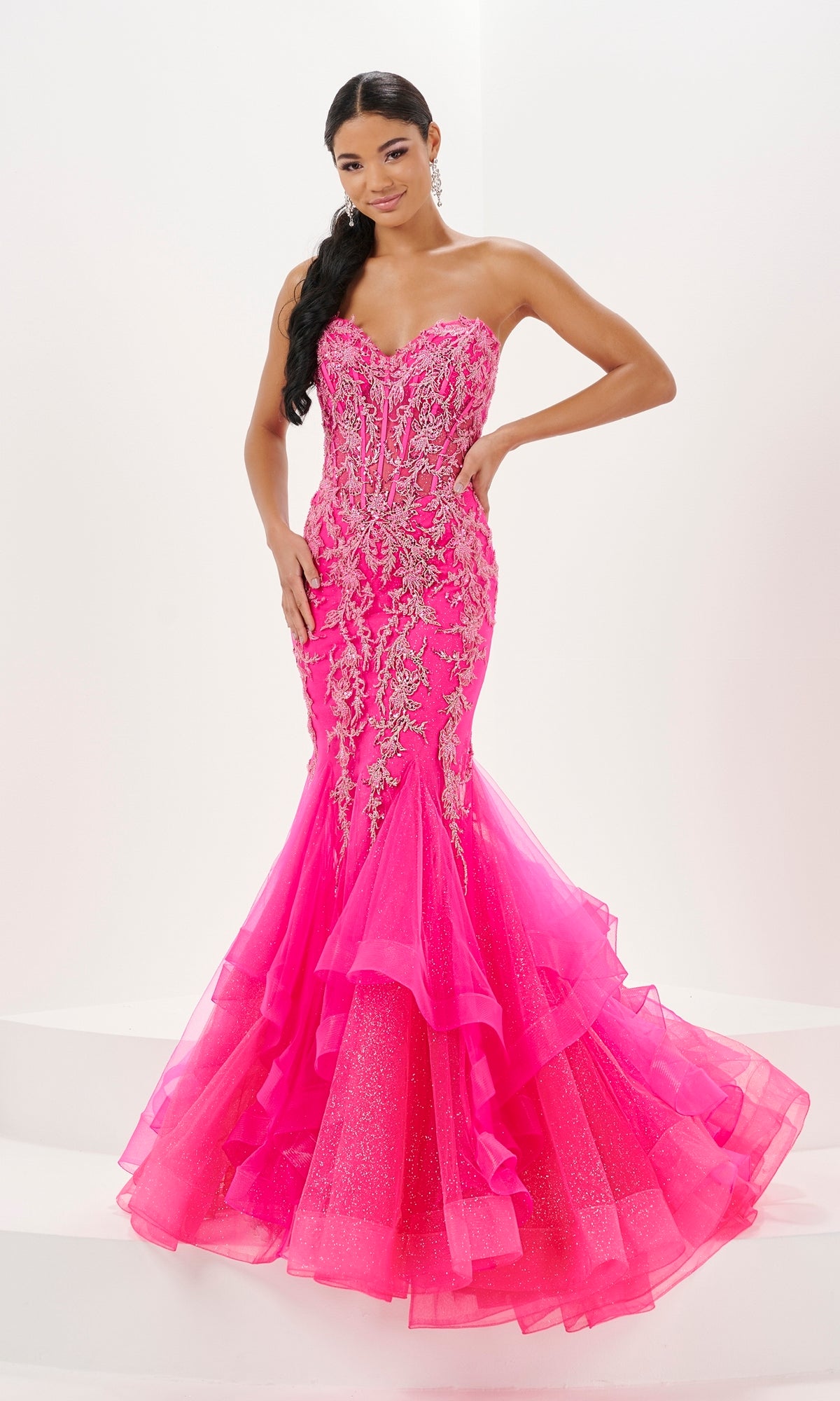 A woman stands against a white background wearing the Long Prom Dress 16057 by Tiffany, a strapless bright pink mermaid gown featuring a sweetheart neckline, silver embellishments, and a layered tulle hem.