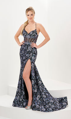 A woman stands with hands on hips, wearing the Long Prom Dress 16060 by Tiffany—featuring a black and purple floral print, spaghetti straps, and a thigh-high slit.