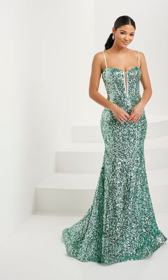 A woman stands indoors wearing the Tiffany V-Neck Fitted Long Sequin Prom Dress 16081—a floor-length green gown featuring corset boning, thin straps, and a sweetheart neckline.