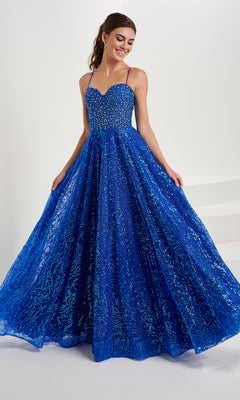 A woman wears the Tiffany Beaded-Bodice Glitter Tulle Prom Dress 16088, featuring a sleeveless royal blue beaded bodice and a full, floor-length glitter tulle skirt, standing against a white background.