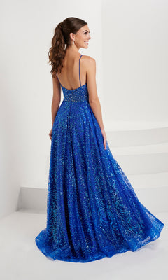 A woman with long brown hair in a ponytail wears the Tiffany Beaded-Bodice Glitter Tulle Prom Dress 16088, featuring an A-line silhouette and thin straps, as she stands on a white floor near white stairs.