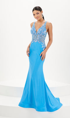 A woman wears the Tiffany Open-Back Floral Jersey Prom Dress 16091, featuring bright blue jersey fabric, a floor-length silhouette, plunging neckline, floral appliques, and silver embellished bodice.