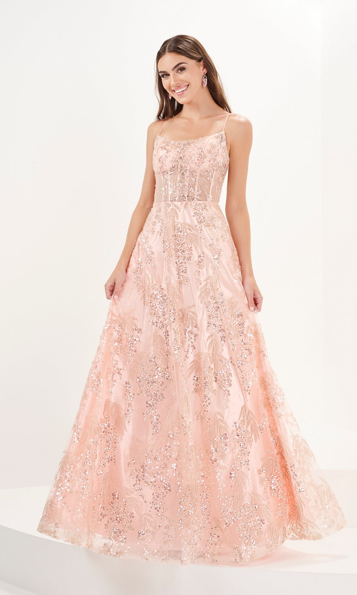 A woman wears the Tiffany Beaded and Sequin Tulle Prom Dress 16093, a sleeveless, floor-length blush pink gown with sequin embellishments, standing against a plain white background.