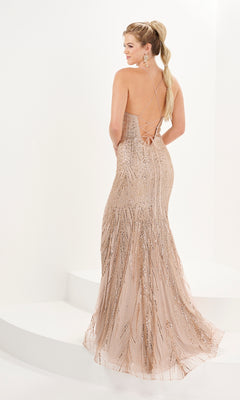A woman stands on white steps wearing the Tiffany Open-Back Glitter-Print Prom Dress 16094, a champagne gown with thin crisscross straps, feather glitter embellishment, sequin detailing, and an open back.
