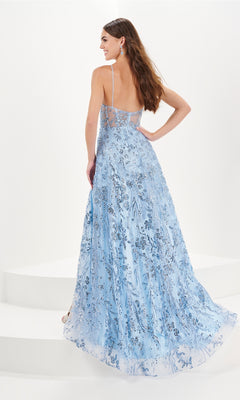 A woman stands on white steps, facing away, wearing the Tiffany A-Line Glitter Tulle Prom Dress 16097 in long light blue with silver floral patterns and a soft a-line silhouette.