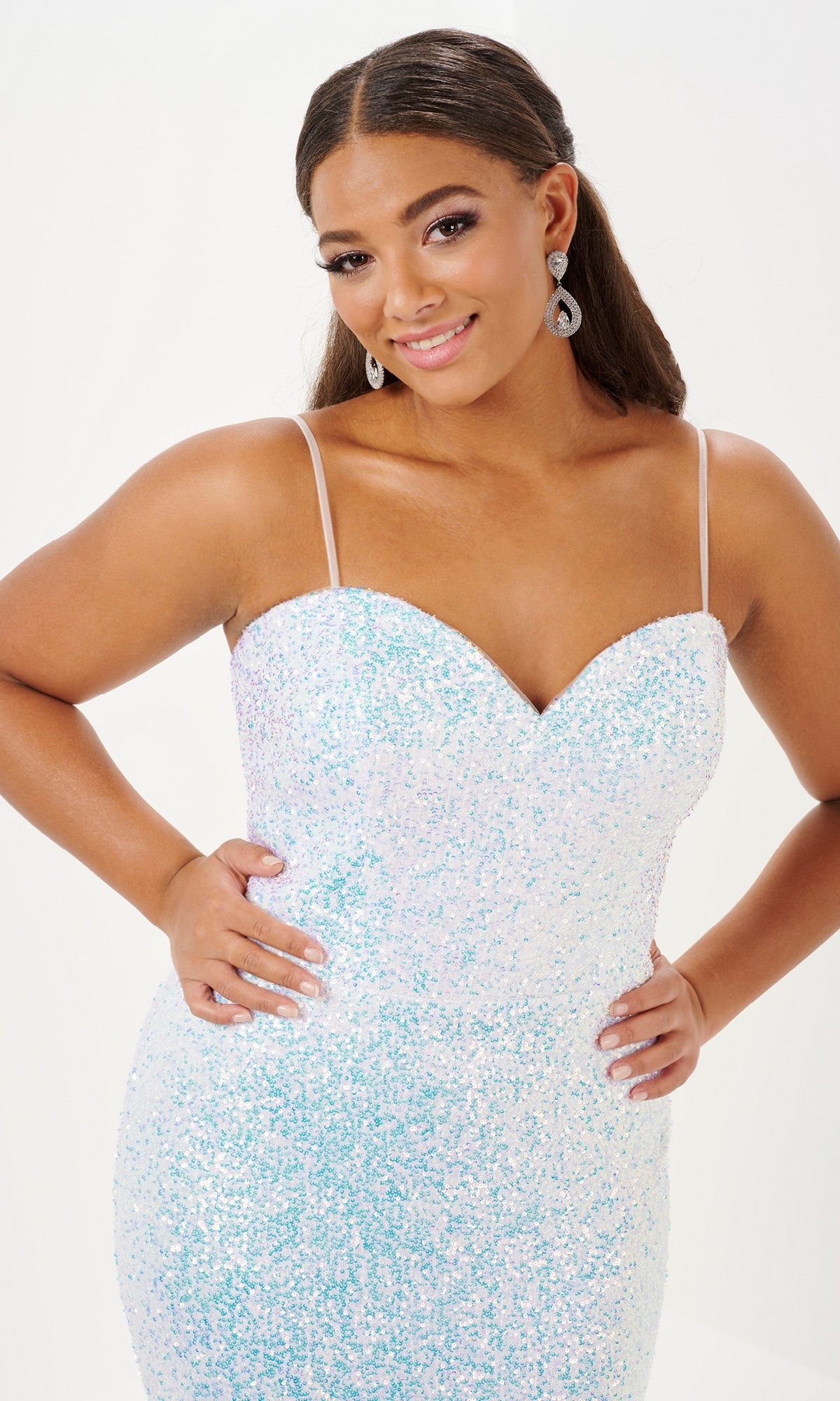 A woman poses with hands on hips in the Tiffany Plus-Size Designer Sequin Prom Dress 16121, featuring a fitted silhouette, thin straps, and a sparkly light blue and white design against a plain background.
