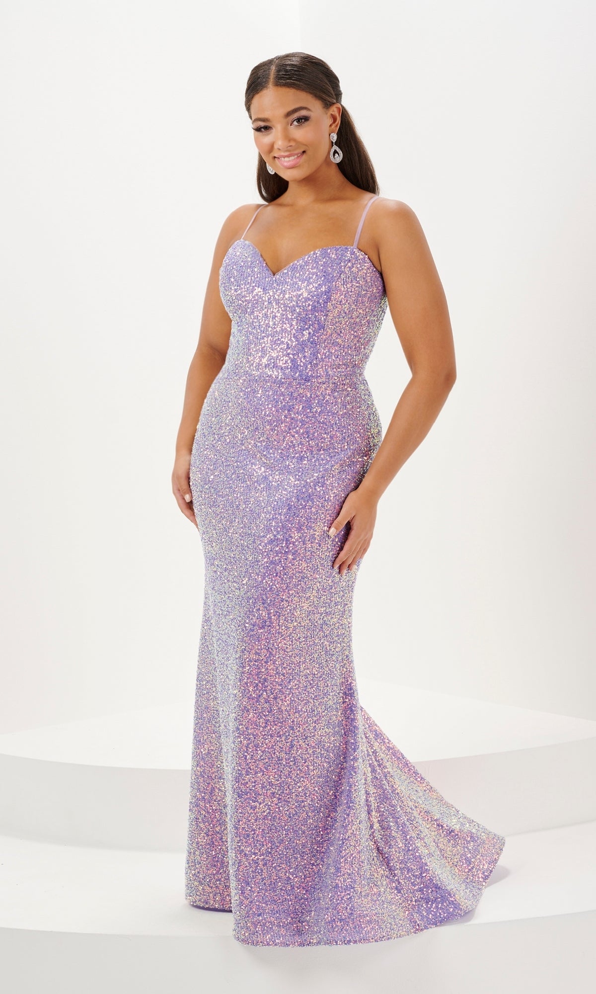 A woman stands smiling against a plain white background, wearing the Tiffany Plus-Size Designer Sequin Prom Dress 16121—a fitted, floor-length lavender gown with glittering sequins, thin straps, and a sweetheart neckline.