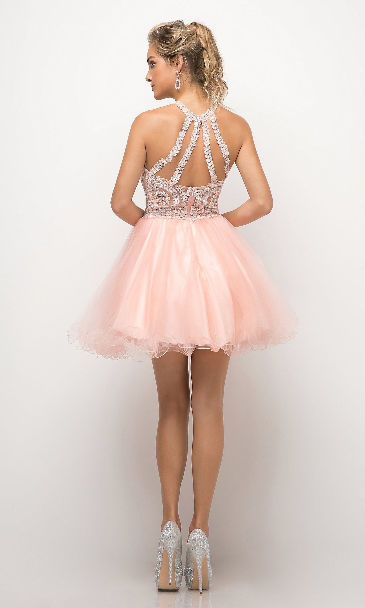 A woman faces away, modeling the affordable High-Neck Short Babydoll Homecoming Dress UJ0119 with a pale pink tulle skirt and embroidered lace bodice, paired with silver heels against a plain white backdrop.