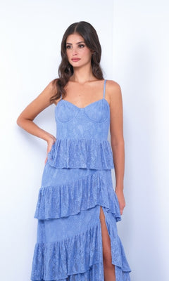 A woman models the Vanna by Velvi: a sleeveless, light blue lace prom dress with tiered ruffles and a thigh-high slit, shown against a plain white background.