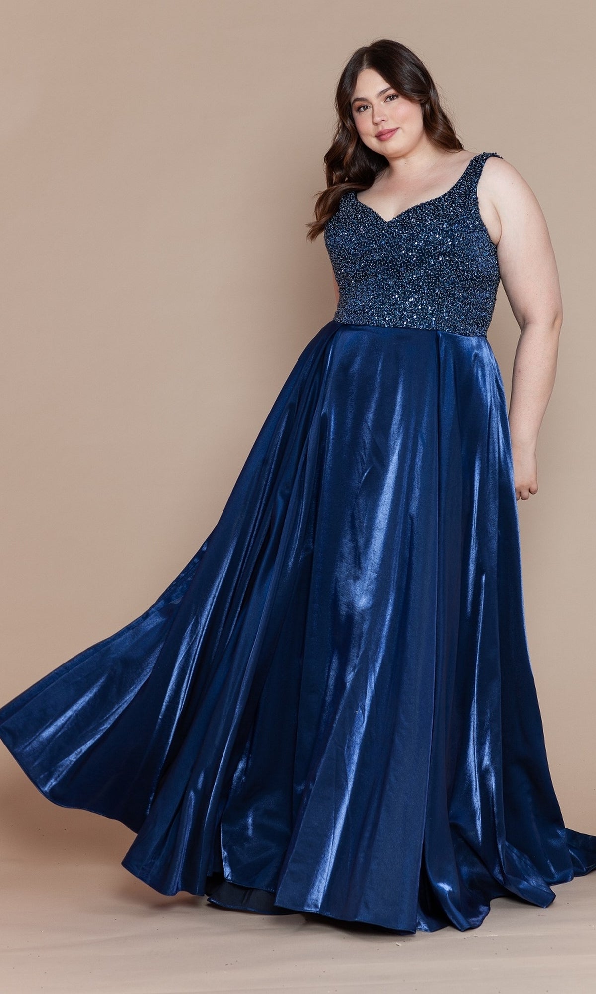 A woman stands against a plain beige background wearing the Beaded-Bodice Plus-Size Long Prom Dress W1066, featuring a sleeveless, navy blue design with a sequined bodice and shiny, flowing skirt.