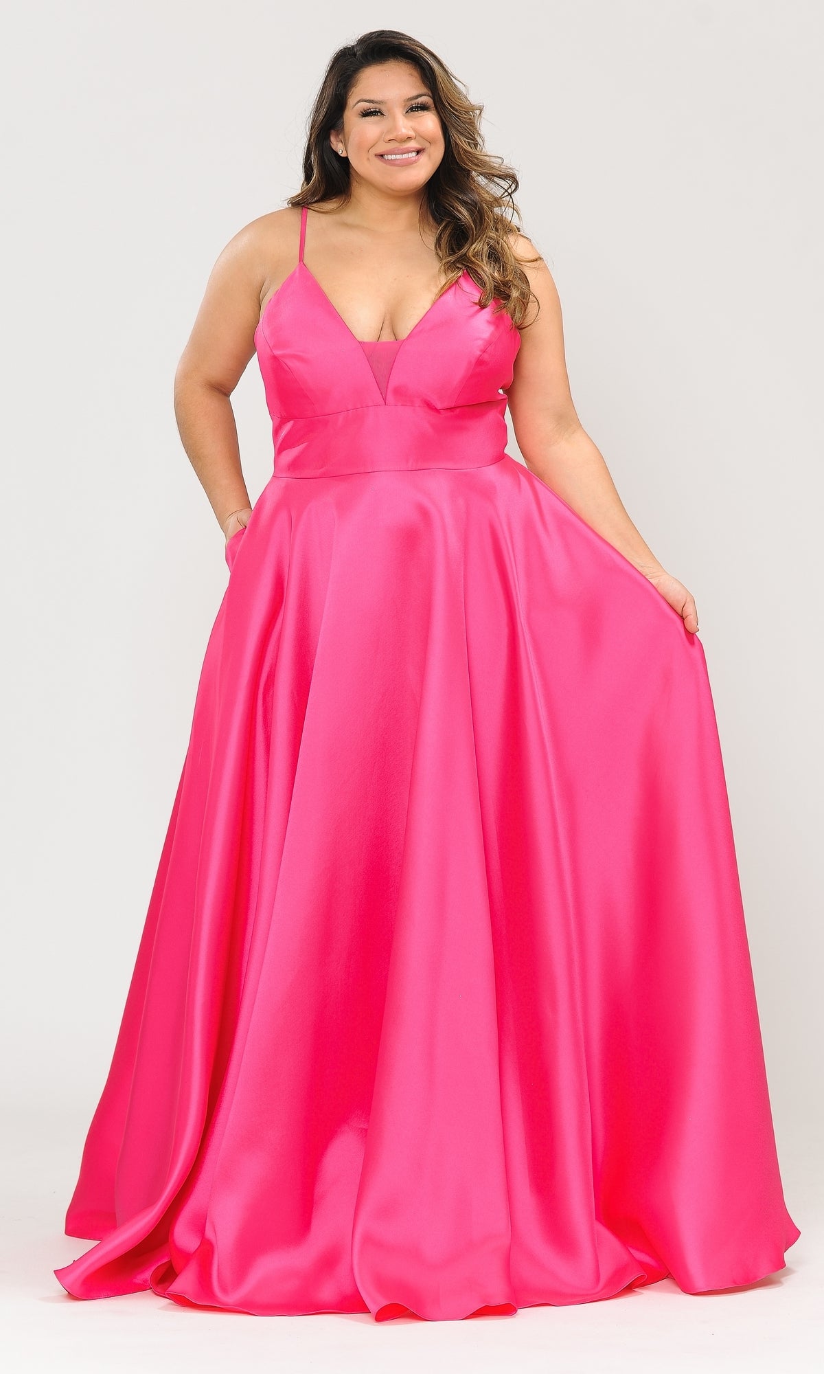 A woman in the Plus-Size Long Corset Prom Dress with Pockets W1070, featuring a bright pink hue and thin straps, stands against a plain light background, holding out the skirt of the fitted gown.