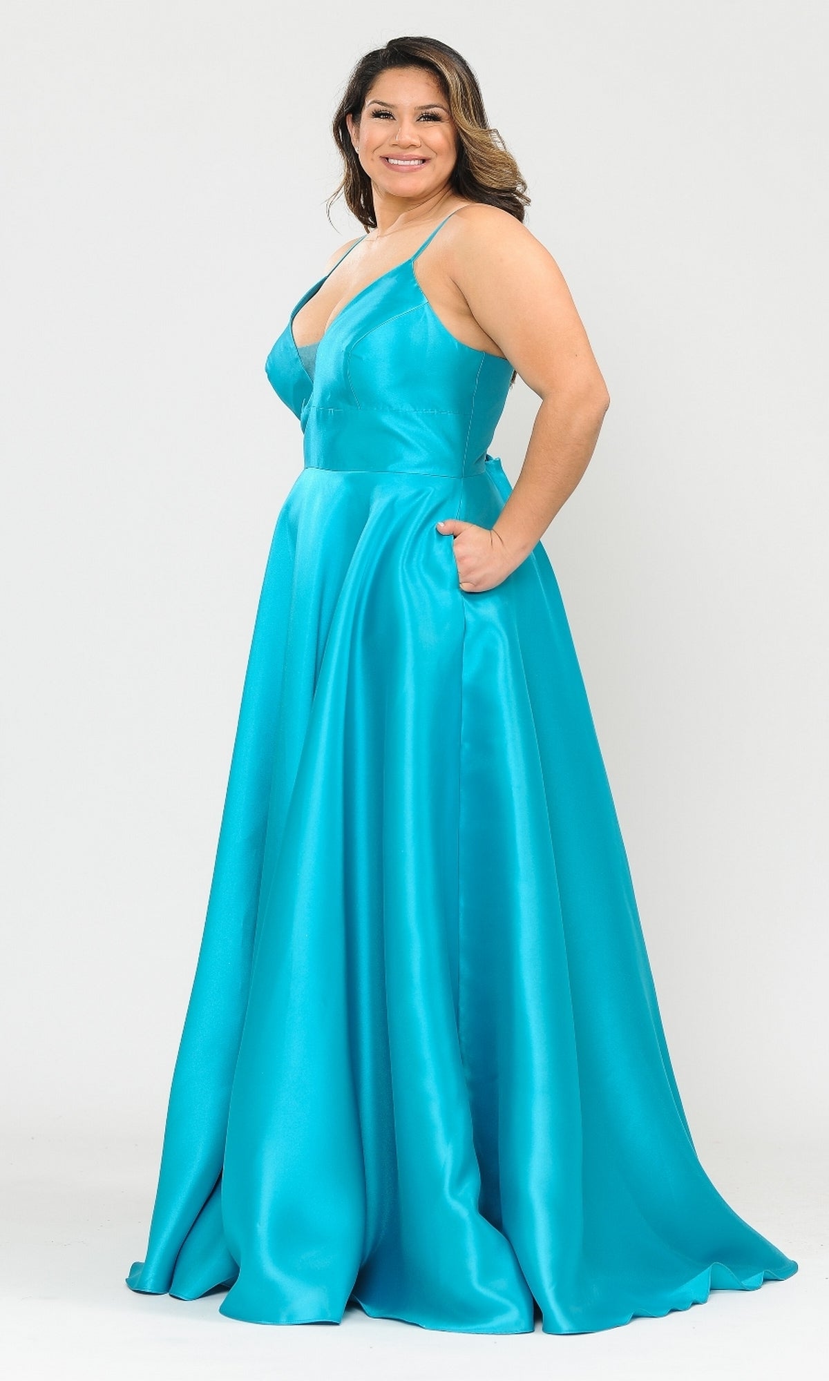 A woman stands smiling in the Plus-Size Long Corset Prom Dress with Pockets W1070—a sleeveless, floor-length turquoise gown—against a plain white background.
