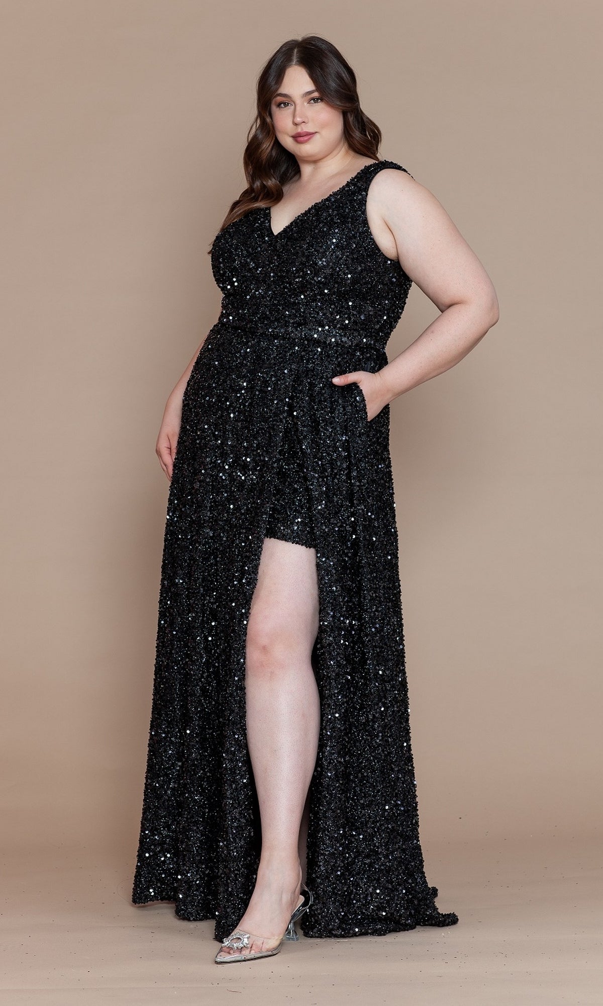 A woman wears the Plus Long Sequin Prom Dress with Underskirt W1128, featuring a black sequin finish, thigh-high slit, and corset-style lace-up back, standing against a plain beige background.