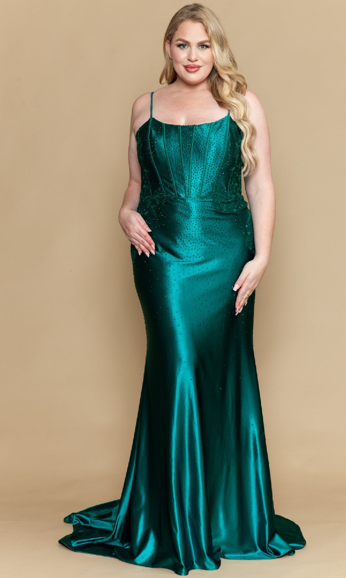 A woman stands on a beige background wearing the PolyUSA W1164, a plus-size, fitted, floor-length emerald green beaded prom dress featuring thin straps and elegant embellishments.
