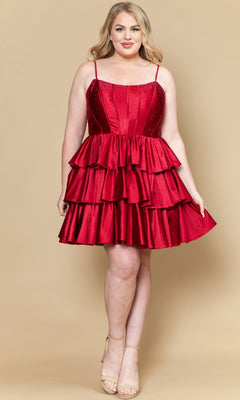 A woman wearing the Short Plus Size Homecoming Dress: Poly USA W1192, a sleeveless red satin dress with tiered ruffles and spaghetti straps, paired with nude heels, stands against a beige background.