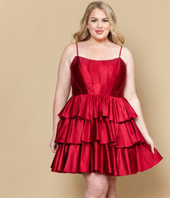 A woman wearing the Short Plus Size Homecoming Dress: Poly USA W1192 in red wine, featuring spaghetti straps and a tiered sleeveless design, stands before a beige background.