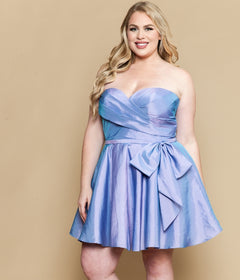 A woman models the Plus-Size Strapless Cocktail Dress: Poly USA W1214 in iridescent lavender with a large waist bow, standing against a beige background.