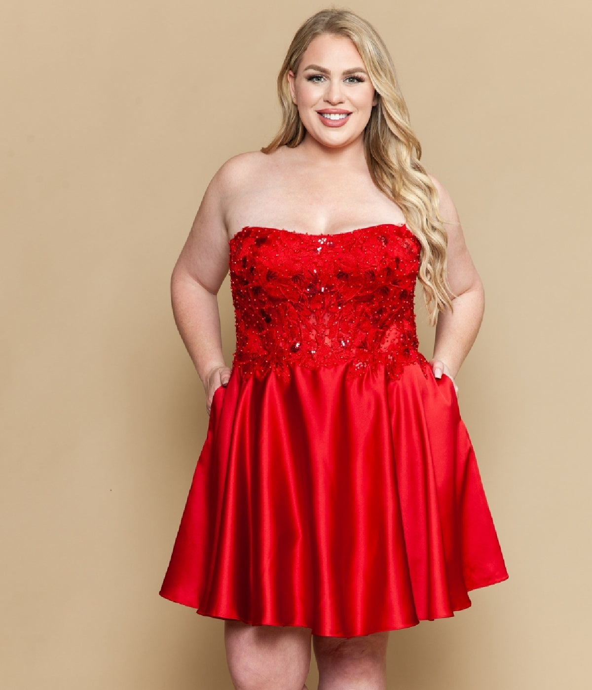 A woman stands against a beige background wearing the Poly USA W1220 plus-size strapless party dress, which features a sequin corset-style bodice, A-line skirt with pockets, and a short silhouette.