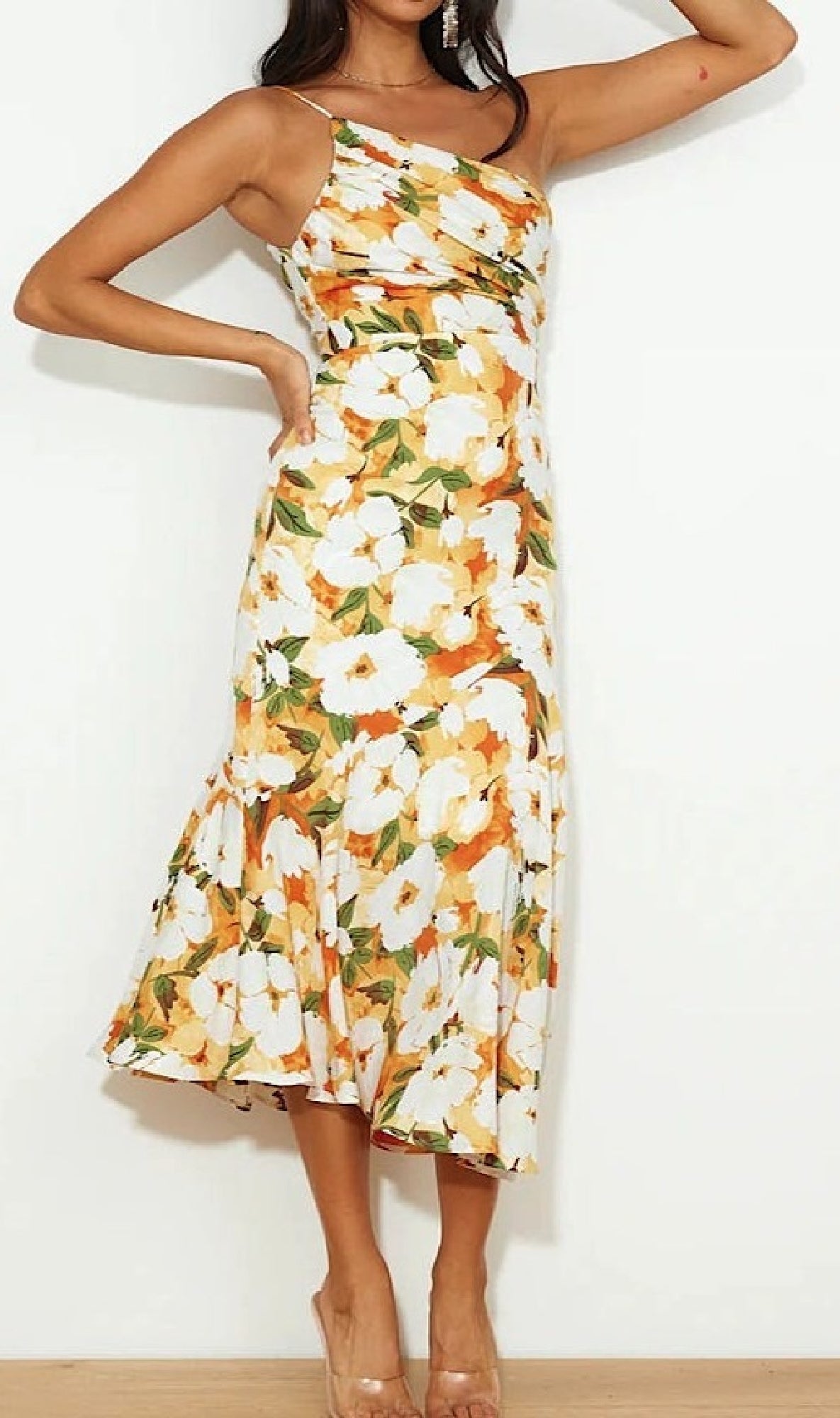 Woman wearing a One-Shoulder Casual Floral Print Midi Dress, featuring orange, yellow, and white flowers, paired with clear high heels, standing against a plain white wall.