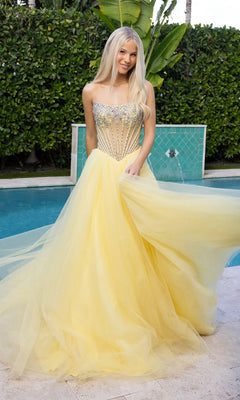 A woman in a yellow Portia and Scarlett XO047 long formal dress with a beaded corset bodice and strapless tulle ball gown skirt stands smiling by a pool, with greenery and blue tile in the background.