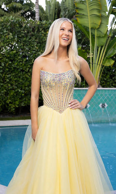 A woman with long blonde hair smiles by a pool, surrounded by green foliage, wearing the Portia and Scarlett XO047 long formal dress featuring a strapless tulle ball gown and beaded corset bodice.
