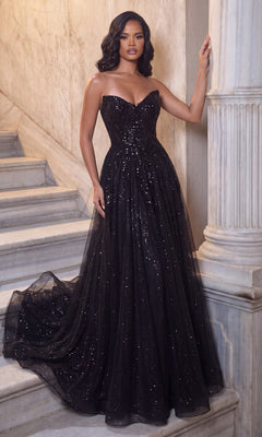 A woman stands on marble stairs wearing the Portia and Scarlett XO134 long formal dress in black, featuring a strapless sweetheart neckline and a sequined, flowing skirt, posing with one hand on a column.