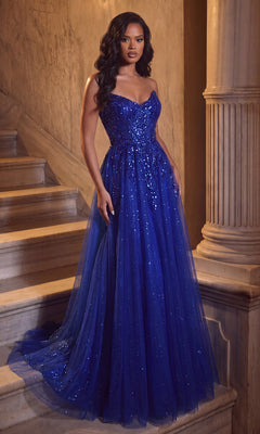 A woman stands on marble stairs near a column, wearing the Portia and Scarlett XO134 long formal dress in cobalt. The strapless evening gown features a sweetheart neckline, sparkling sequin embellishments, and a flowing tulle overlay that extends to the floor.